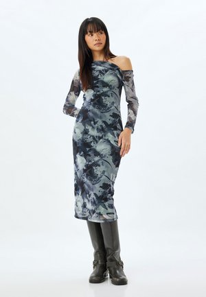 Robe à imprimé floral sombre avec un design décolleté et de longues manches transparentes, confectionnée dans un tissu léger, accompagnée de bottes noires montantes.