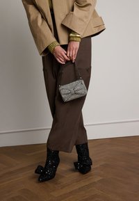 Pantaloni beige a gamba larga abbinati a una giacca oversize beige, un maglione in maglia verde e stivaletti neri con paillettes. Una piccola borsa a scacchi completa il look.