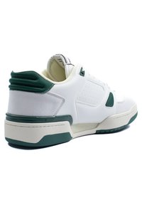 Bijele tenisice s zelenim naglascima, izrađene od kože i suede materijala, s podstavljenim ovratnikom, perforiranim stranama i teksturiranom gumiranom potplatom.