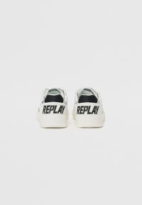 Baskets blanches avec une finition métallique, présentant un logo noir "REPLAY" sur le talon arrière et une surface texturée. Design à semelle plate.