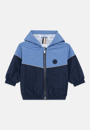 Dječja jakna s kapuljačom u tamnoplavoj i svijetloplavoj boji s prednjim patentnim zatvaračem, elastičnim manšetama, bočnim džepovima i naljepnicom s logotipom na prsima.