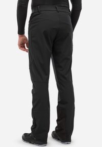 Czarne, wodoodporne spodnie o eleganckim fasonie, z wyprofilowanymi kolanami i zamykanymi nogawkami, w połączeniu z wytrzymałym czarnym obuwiem.