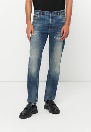 Blue denim jeans with a faded wash, featuring distressed details and a straight leg design. Paired with black slip-on shoes.