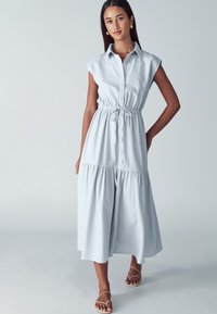 Abito senza maniche di un blu chiaro, con chiusura frontale a bottoni, vita con cordoncino e un design di gonna a strati. Tessuto morbido con un aspetto casual.