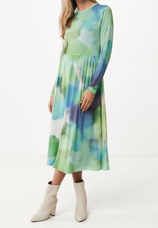 Femme portant une robe tie-dye à manches longues, longueur mollet, dans des nuances de vert, bleu et blanc, associée à des bottines blanches.