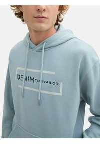 Sudadera de algodón azul claro con cordones, que presenta el texto negro "DENIM tom tailor" y un gráfico rectangular en blanco.