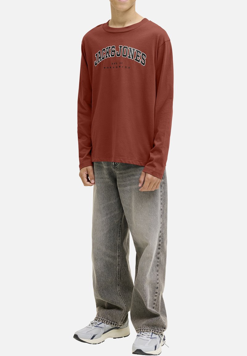 T-shirt rouge à manches longues avec "JACK & JONES" imprimé en noir sur la poitrine, associé à un jean gris ample et des chaussures de sport blanches.