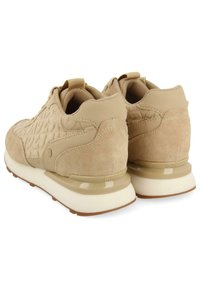 Zapatillas de ante beige con detalles texturizados, cuello acolchado y suela de goma blanca. Presentan un logo sutil en el lateral y una forma redondeada.