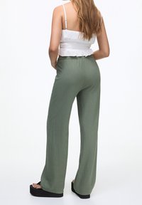 Pantalon vert clair à jambes larges, fabriqué en tissu doux à texture lisse, avec une taille élastique. Associé à un crop top blanc smocké.
