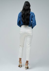 Pantalones de denim blanco con un corte recto y bolsillos traseros, combinados con una camisa de denim azul, llevados con sandalias de tacón beige.