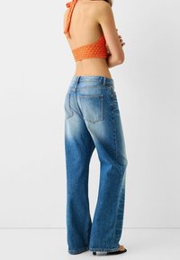 Jeans de denim de pierna ancha y alta cintura en un lavado azul claro, que cuentan con bolsillos traseros cosidos y un corte relajado, combinados con un top corto naranja.