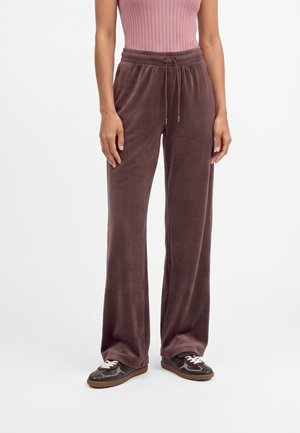 Person wearing brown wide-leg velour pants with an elastic waistband and black casual sneakers with white laces.