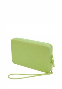 Funda verde de goma con cremallera y superficie texturizada, logo de Havaianas y una correa de muñeca para un fácil transporte. Diseño rectangular.