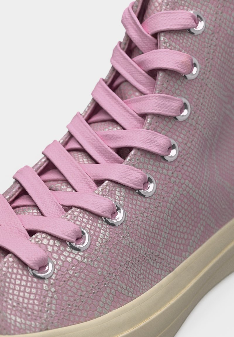Roze sneaker met een gestructureerd slangenhuidpatroon, roze platte veters geregen door zilverkleurige veteroogjes en een beige rubberen zool.