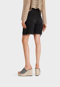 Pantaloni shorts in denim nero con orlo sfilacciato, abbinati a sandali con zeppa a motivi bianchi e neri, dotati di tacco in giuta intrecciato e design con punta aperta.