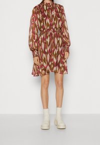 Kort klänning med puffärmar och mönster i flerfärgade ikatnyanser av rosa, brun och krämfärgad, med en samlad midja och mjuk, flödande tyg.