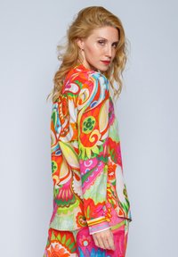 Buntes Langarmoberteil mit einem lebhaften Blumenmuster in Rot, Pink, Grün und Gelb, aus glattem Stoff und mit kontrastierenden Bündchen.