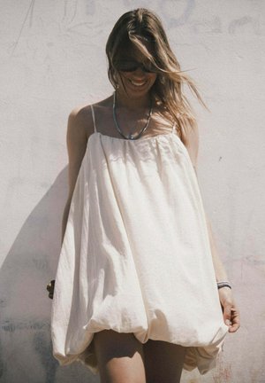 Helles cremefarbenes Baumwollkleid mit lockerem Ballonschnitt und dünnen Trägern. Verfügt über eine geraffte Taille und reicht knapp über die Knie.