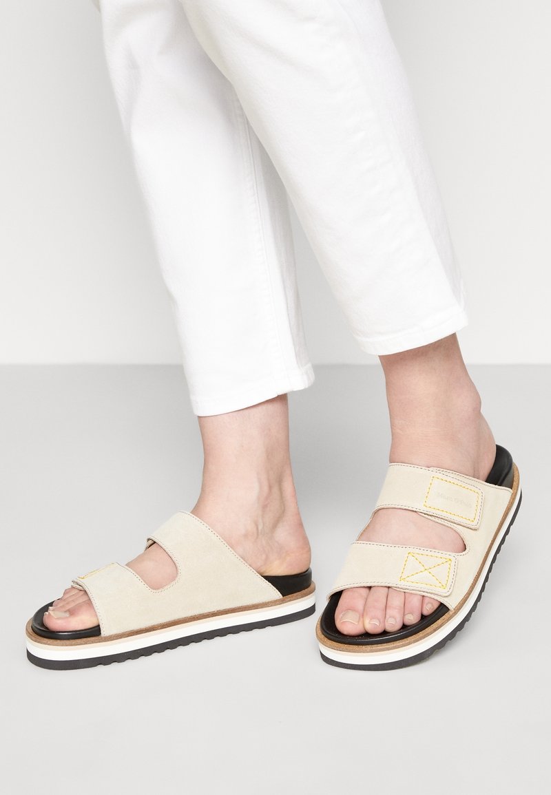 Beige slidesandaler med to brede stropper, kontrasterende gule syninger, gummisål og let forhøjet design for komfort.