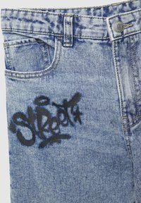 Jeans in denim azzurro chiaro con un logo "Street" in stile graffiti nero ben distinto sul davanti, design tradizionale a cinque tasche e bottone in metallo.