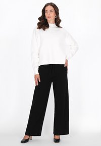 Pullover bianco con un collo alto, decorato con delicate scintille sulle spalle, abbinato a pantaloni neri larghi e tacchi.