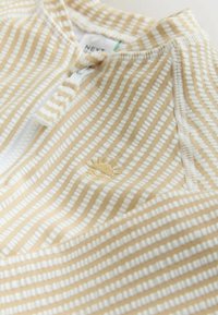 Krém és bézs csíkos ing, fél cipzárral, puha anyagból, a mellkason nap motívummal.