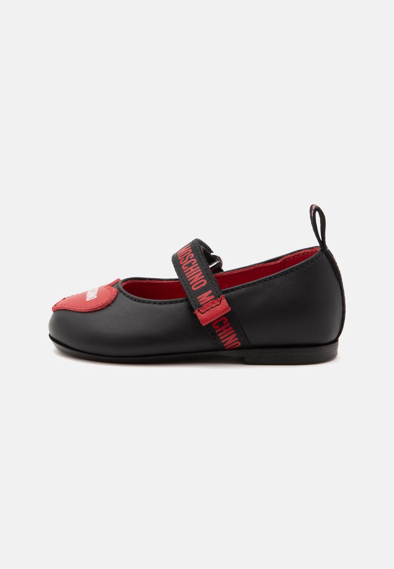 Chaussure Mary Jane noire avec un détail cœur rouge sur l’orteil et une bride noire avec le texte rouge « Moschino », semelle plate et languette de tirage au talon.