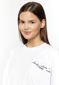 Witte sweatshirt met ronde hals, met geborduurde wolken en zon, en de tekst "buiten bewolkt, binnen blij." Zachte textuur.