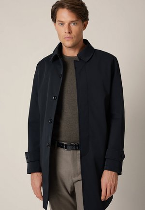 Granatowy płaszcz o dopasowanym kroju, wykonany z gładkiego materiału. Posiada spiczasty kołnierz, zapięcie na guziki oraz podwinięte mankiety. Klasyczna sylwetka.