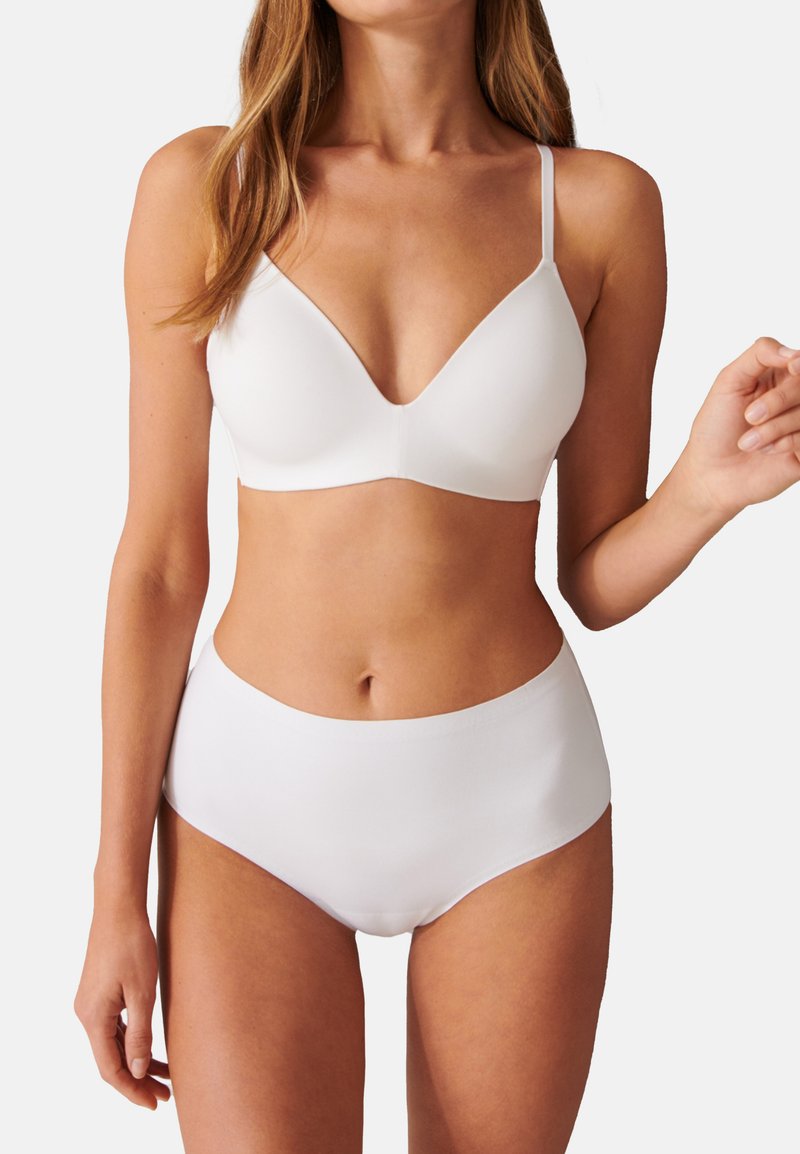 Vit sömlös bralette med justerbara remmar och djup V-ringning, i kombination med högmidjade vita bikiniunderbyxor. Slät, elastisk tyg.