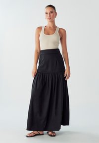 Gonna maxi nera con design a strati e vita aderente, abbinata a un top a canotta a coste beige chiaro e sandali neri con cinturini.