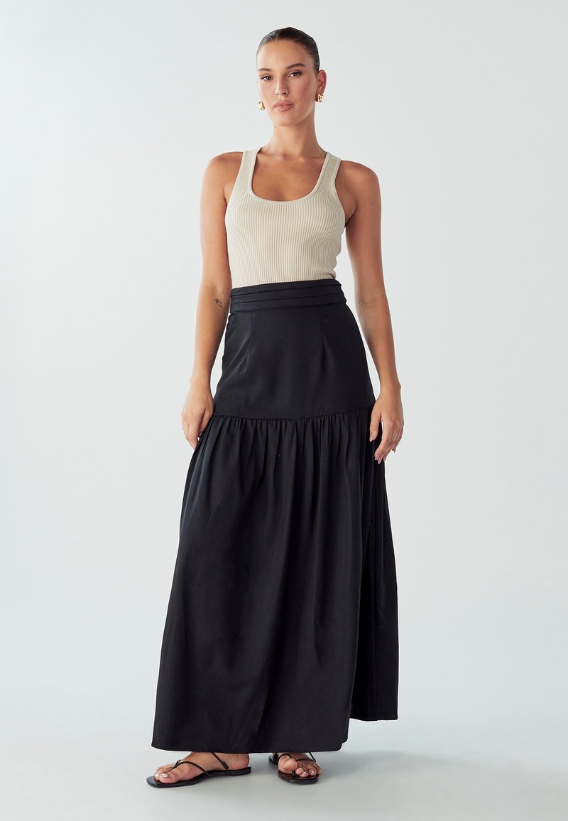 Gonna maxi nera con design a strati e vita aderente, abbinata a un top a canotta a coste beige chiaro e sandali neri con cinturini.