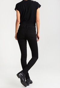 Jeans skinny negros de algodón con una cintura alta, que presentan una textura suave y bolsillos traseros sencillos. Combinados con una blusa negra ajustada y botas de tobillo.
