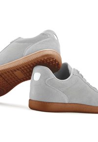 Graue Wildleder-Sneaker mit texturierten, braunen Gummisohlen. Merkmale sind ein geschmeidiges Design, kontrastierende weiße Akzente und ein minimalistischer Look.