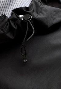 Gros plan sur un tissu noir avec un bloque-cordon rond et un cordon de serrage ajustable.