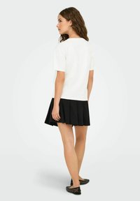 Witte top met korte mouwen gecombineerd met een zwarte plissérok. De outfit heeft een eenvoudig ontwerp, met een gladde stof en een ontspannen pasvorm.