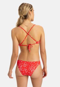 Red bikini set with white floral patterns, featuring a crisscross back design and a tied closure. Material appears smooth and stretchy.