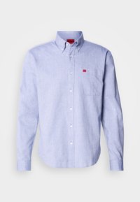Chemise bleu clair à manches longues avec boutons, poche poitrine et étiquette de marque rouge sur la poche et à l'intérieur du col.