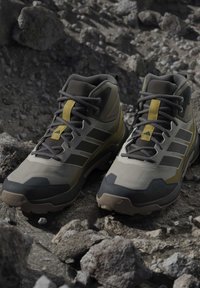 Ζευγάρι γκρι και κίτρινων ορειβατικών μποτών με μαύρα κορδόνια που ακουμπούν σε βραχώδη περιοχή.