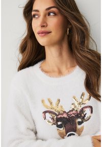 Witte, pluizige trui met een rendierontwerp versierd met pailletten. Opvallende details: gouden en rozenkleurige accenten, ronde halslijn en zachte textuur.