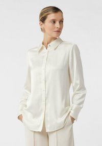 Satin white long-sleeve shirt with a button-up front, classic collar, and side pockets. Smooth texture and a relaxed fit.