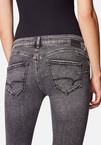Harmaan pesun denim-farkut, joissa on slim fit -malli, takataskut ompelutiedoilla ja pieni logo-tunnus vyötärön lähellä.