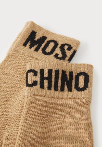 Beige strikkede sokker med sort skrift "MOSCHINO" og "CHINO" på kanten, med et struktureret stof og en ribbet design.