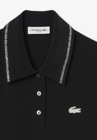 Zwarte polo met een kraag, versierd met strass steentjes langs de kraag en een in zilver geborduurd Lacoste-logo.