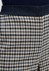 Tkané kalhoty s vzorem houndstooth v námořnické modré a krémové barvě, s tmavě modrým pasem z denimu. Textura vypadá hladce a má strukturovaný tvar.