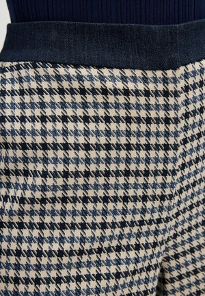 Geweven stof broek met houndstooth patroon in marineblauw en crème, met een donkere denim tailleband. De textuur lijkt glad met een gestructureerde vorm.