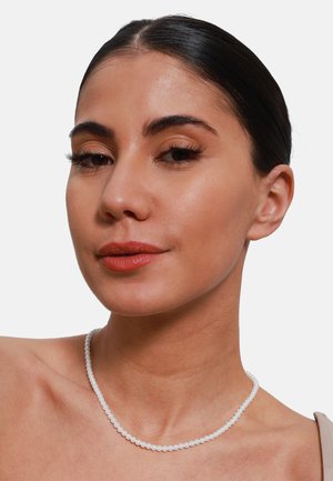 Perlenkette mit kleinen, runden weißen Perlen, die aufgezogen sind. Der Hautton ist hell, mit einer glatten Textur und natürlichem Make-up.