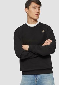 Zwarte sweatshirt van katoen met lange mouwen en een ronde hals. Er is een klein logo op de bovenste linkerkant.