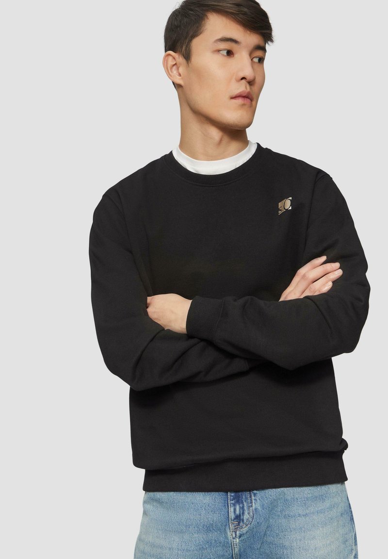 Zwarte sweatshirt van katoen met lange mouwen en een ronde hals. Er is een klein logo op de bovenste linkerkant.