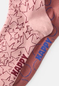 Meias até ao joelho em rosa e terracota com padrões de estrelas e a palavra "FELIZ" em cores contrastantes. Feitas de um material suave e texturizado.